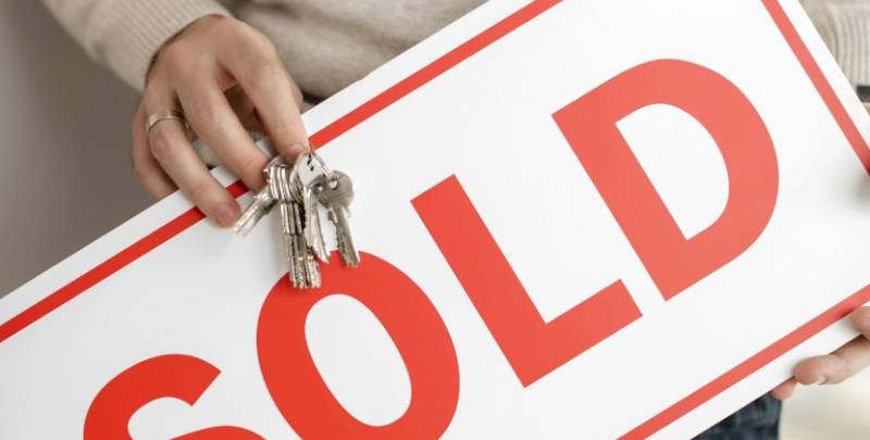 A person holds a sign that says 'sold' and some keys